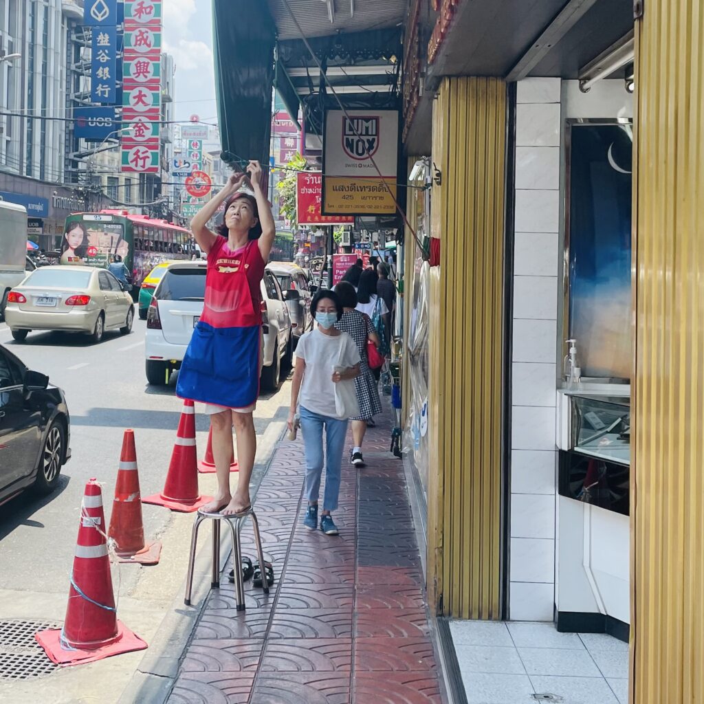 Thaïlandaise sur un tabouret fixant une lampe devant sa boutique de Chinatown à Bangkok en Thaïlande